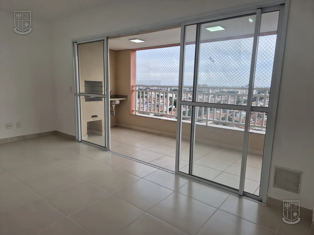 Sala ampla e vazia, com porta de vidro para a varanda e a cidade ao fundo.