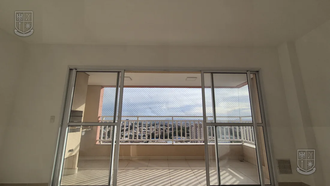 Sala ampla e vazia, com a porta de vidro da varanda aberta para a cidade.